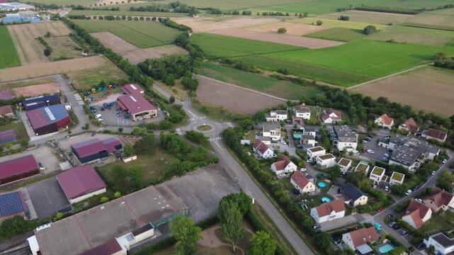 Aerial view of Dambach-La-Ville, France. Tracking shot over houses and commercial buildings in a rural landscape during summer, finally tilting over a roundabout.