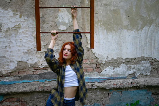 Red-haired woman in casual clothing near old wall with destroyed facade