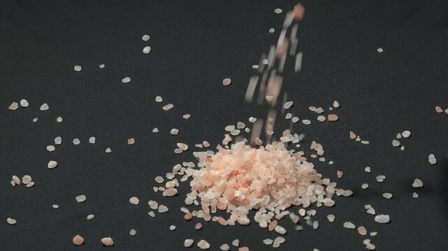 Slow motion action of pure pink Himalayan salt crystals falling on a black background. Premium natural mineral for healthy cooking and spa treatments.