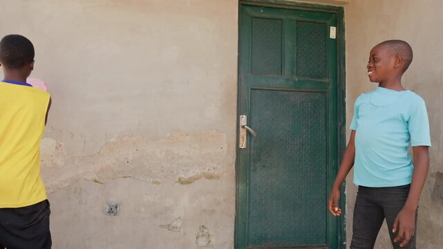 Two black boys volleying pink balloon by green door, spirited duel with tosses, reactive catches and laughter, one in yellow one in turquoise, urban backyard vibe, energetic motion and friendly