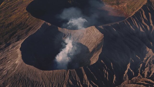 Aerial view of the Bromo volcano's crater, with smoke rising from it, showcasing the stark textures of the volcanic landscape, Bromo Tengger Semeru National Park, East Java, Indonesia.