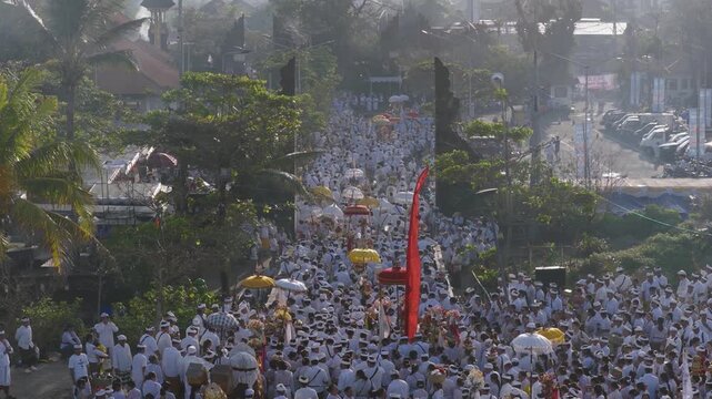 Seminyak, Indonesia - 21 March 2026: Aerial view of a bustling procession with white parasols winding through the town, a vibrant display of culture.