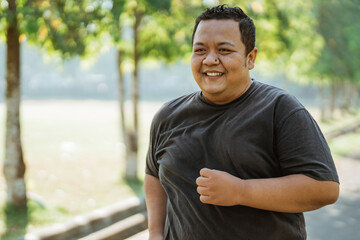 Fototapeta premium portrait of a fat man with a toothy smile jogging in the morning while exercising in the park