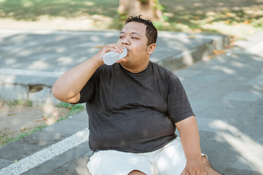 fat man sits drinking mineral water after exercise to lose weight in the park