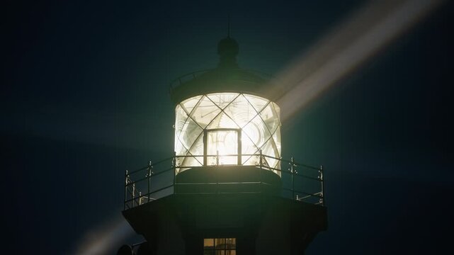 Close up view of Point Cabrillo Lighthouse lantern glowing through light fog at night, bright rotating beam illuminating glass structure above Mendocino, California, USA creating dramatic atmosphere
