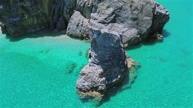 Cinematic drone orbit shot of the iconic Mylopotamos beach in Pelion. High-angle view of the natural rock arch, turquoise Aegean waters and golden sand. Stunning coastal panorama. No audio.