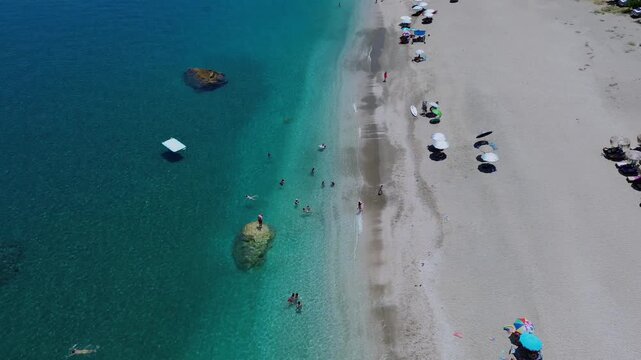 Cinematic drone shot of Agii Saranta beach in Pelion. High-angle view of the white sand, turquoise water and lush green cliffs meeting the Aegean sea. Ideal for travel and tourism storytelling.