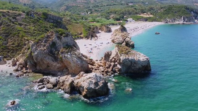 Cinematic drone shot of the iconic giant rocks at Potistika beach in Pelion. High-angle view of turquoise Aegean waters, golden sand and lush green hills. Ideal for travel and tourism promos.