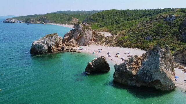 Cinematic drone orbit shot of the iconic giant rocks at Potistika beach in Pelion. High-angle view of turquoise Aegean waters, golden sand and lush green hills. Ideal for travel and tourism promos.