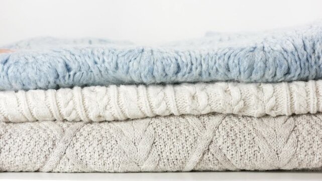 Woman hand selecting cozy sweaters stacked in neutral colors. Cozy sweaters concept shows soft textile, warm clothing choice, minimal style, seasonal wardrobe and comfortable lifestyle.