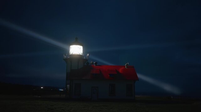 Lighthouse beacon shining over dark ocean with fog and mist near Mendocino, California, USA, creating strong contrast light rays and dramatic coastal night atmosphere