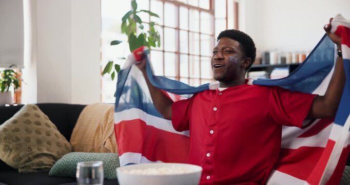 Celebration, flag of United Kingdom and shouting with black man watching tv in home living room. Great Britain, scream and support with excited fan in apartment for streaming or subscription