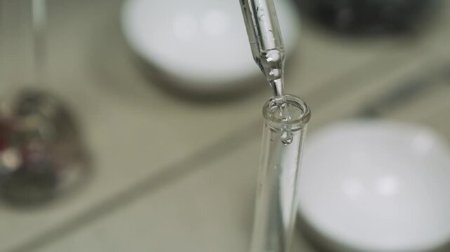 Close-up of liquid dripping from pipette into chemistry beaker. Medical laboratory test, pipette drips transparent chemicals into test tubes. Chemical analysis of liquid.