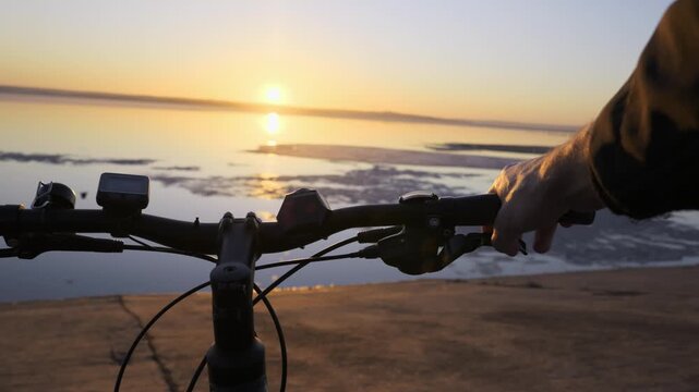 A cyclist rests their hand on bicycle handlebars while pausing to admire a calm lake during sunset. Concept of outdoor exploration, active lifestyle, and finding peace in nature.
