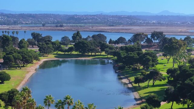 Aerial view of Mission Bay Park island featuring serene blue lake surrounded by vibrant green grass and mature trees.