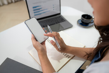 Fototapeta premium Person Using Smartphone and Writing in Notebook at Workspace