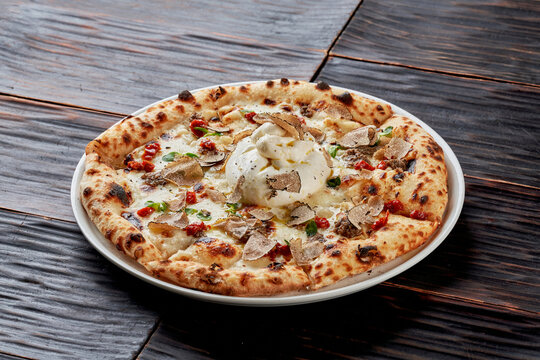 Gourmet Neapolitan pizza topped with creamy burrata cheese, black truffle slices, and sun-dried tomatoes on a dark wooden background. Luxury dining.
