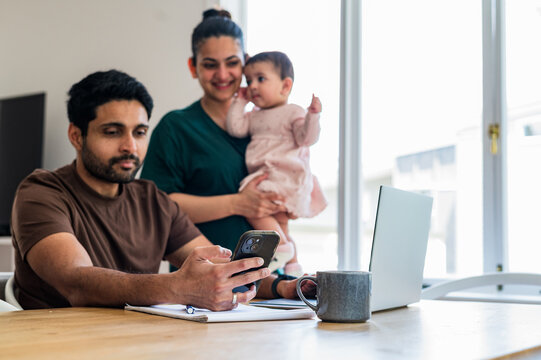 Indian man looking on his phone while woman stands beside him holding baby girl