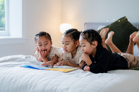 Young kids lying on their belly on the bed reading a colourful storybook