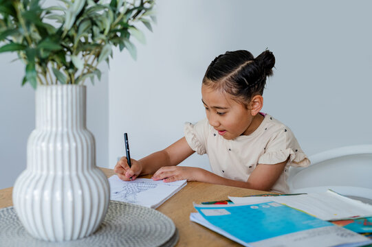 Young Samoan girl sitting behind wooden table doing her homework