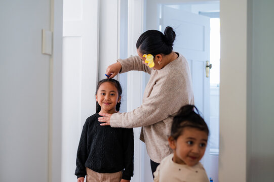 Young Samoan boy with braided hair standing against the wall while mum measures his height