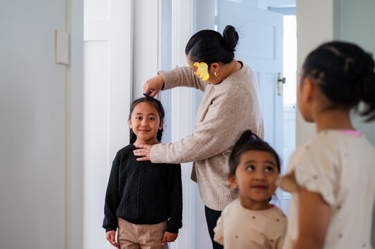 Young Samoan boy with braided hair standing against the wall while mum measures his height