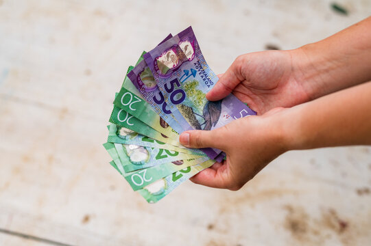 Hands holding various New Zealand banknotes showing a twenty and fifty, two hundred twenty in total