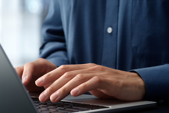 Businessman using laptop computer at desk in office. Closeup of hands and keyboard. Business technologies.