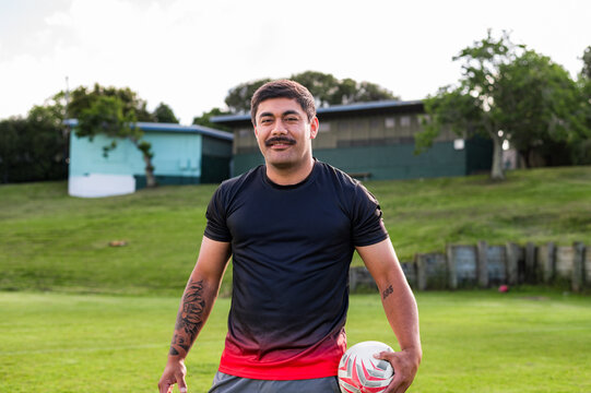 Rugby player stands on the field, smiling while holding a ball, ready for practice