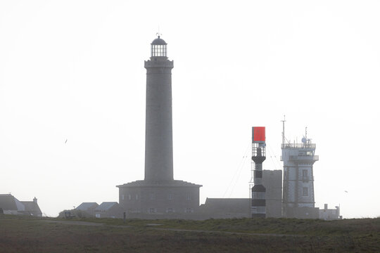 View of Phare d'Eckmuhl lighthouse and maritime signal towers standing against a misty sky Penmarch, Bretagne, France.