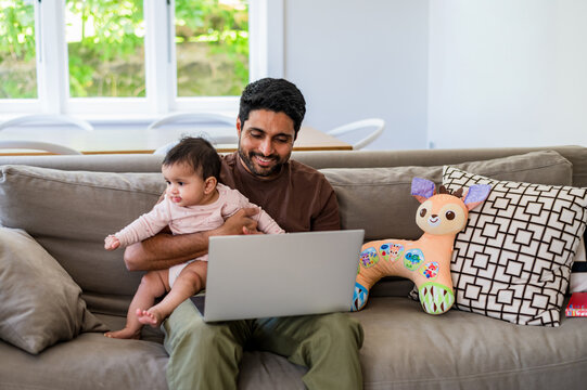 Parent using laptop while holding baby