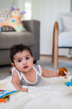 Baby girl crawling and exploring different toys on a soft blanket in a living room