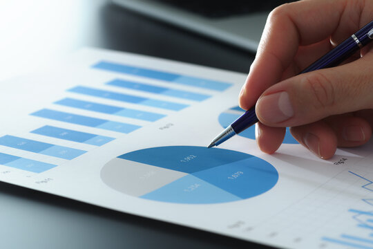 Market research reports with graphs and pie charts. Statistical marketing analysis of target segment. Close-up of businessman's hand and survey results data.