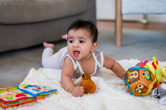 Baby girl crawling and exploring different toys on a soft blanket in a living room