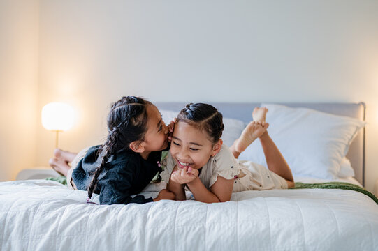Young boy whispering on sisters ear while lying on their belly on the bed