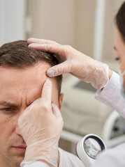 Fototapeta premium Dermatologist examining a man's receding hairline in clinic