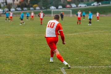 Soccer player wearing a red and white uniform on a grassy field in a rural football game, illustrative image. © kovop58