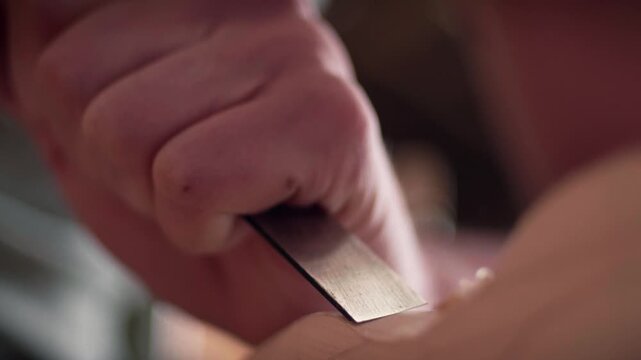 Female artisan craftsman's hands carefully using a sharp metal chisel to shape a piece of light-colored wood in a carpentry workshop. Slow motion.