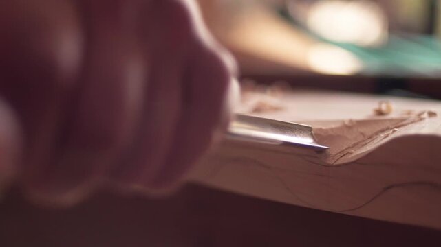 Wood shavings curling off a timber block as a female carpenter uses a manual chisel tool. Slow motion detail shot.