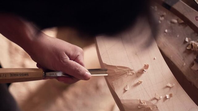Female artisan woodworker shaping a piece of timber using a handheld chisel tool. Detailed view of wood shavings being removed in slow motion.