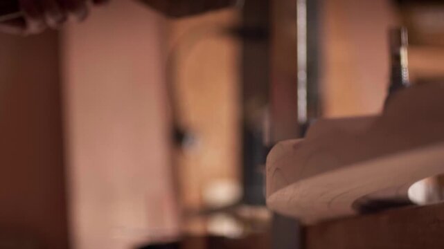 Skilled artisan uses a sharp metal chisel to shape a curved piece of timber in a workshop. Slow motion shot highlights the precision of manual woodworking.