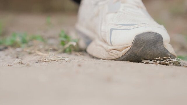 White sneaker toe pushing forward on dusty soil closeup showing forefoot contact with ground, tiny pebbles and plants, forward momentum, low angle perspective, action rhythm and tactile texture