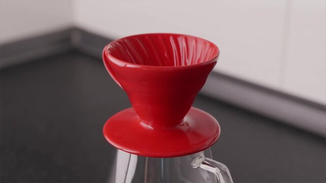Close-up of hands setting up red V60 dripper on glass carafe