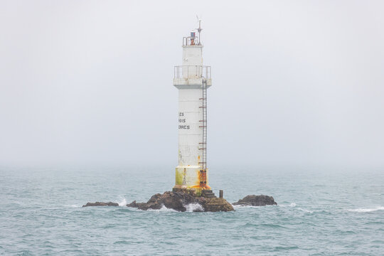 View of Les Trois Pierres lighthouse standing on a rocky outcrop amidst misty sea waters in Ushant, Brittany, France.