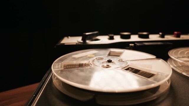 Vintage reel-to-reel tape recorder spins magnetic audio tape in a dark room as smoke slowly drifts across the machine. The atmospheric scene represents a nostalgic concept of classic analog sound