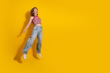 Fototapeta premium Cheerful young woman in striped top posing playfully on a vibrant yellow background, showcasing casual and trendy summer style