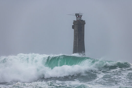 View of Nividic Lighthouse standing amidst powerful breaking waves and misty weather in Ushant, Brittany, France.