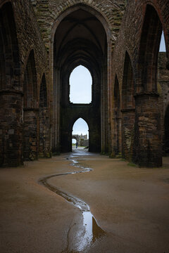 View of the Gothic arches and stone ruins of the Abbey of Saint-Mathieu with a winding puddle on the sandy floor in Plougonvelin, Brittany, France.