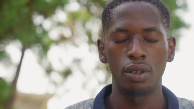 Black man boxer meditative breathing outdoors, eyes closed with sweat, focused on mental toughness and strategy between rounds, quiet concentration under trees, firm jaw and steady rhythm of breath