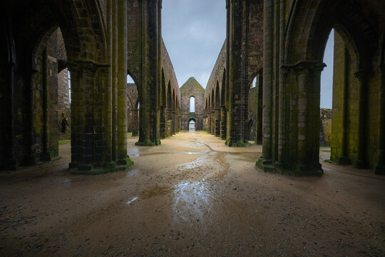 View of the ruined Abbey of Saint-Mathieu at Pointe Saint-Mathieu with moss-covered stone pillars and a sandy floor in Plougonvelin, Brittany, France.